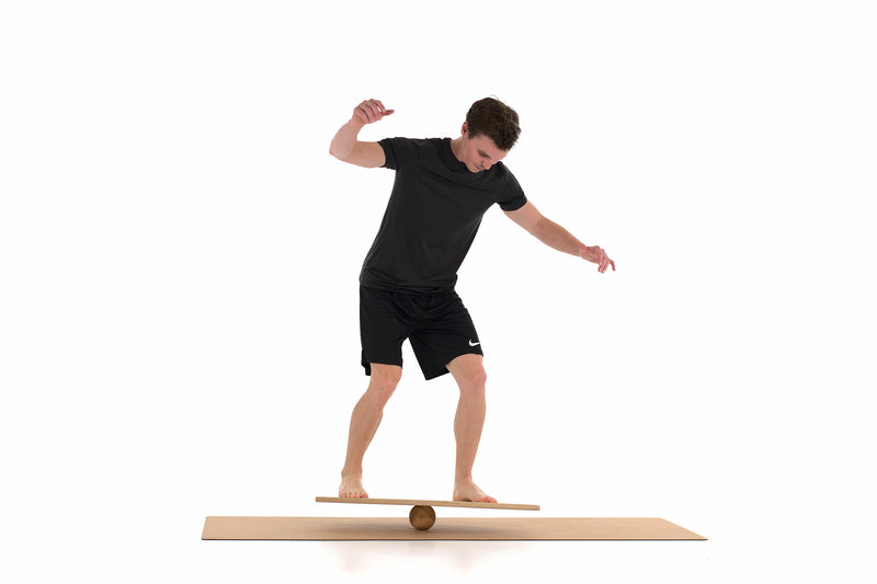 Ein Mann surft auf einem Balance Board von Rollholz, das auf einer Massagekugel liegt. Die Unterlage bietet eine Korkmatte.