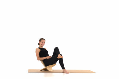 Eine Frau sitzt auf einem als Hocker zusammengebauten Balance Board. Die Unterlage bietet eine Korkmatte von rollholz.