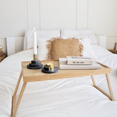 Kerzenständer in grau und gold mit Kerze auf Holztisch auf einem Bett
